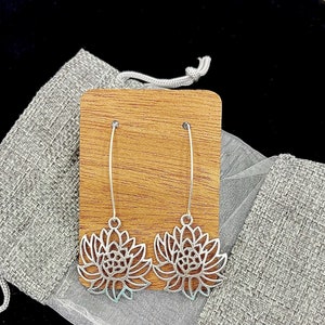 May include: A pair of silver dangle earrings with a delicate flower design. The earrings are displayed on a wooden stand.