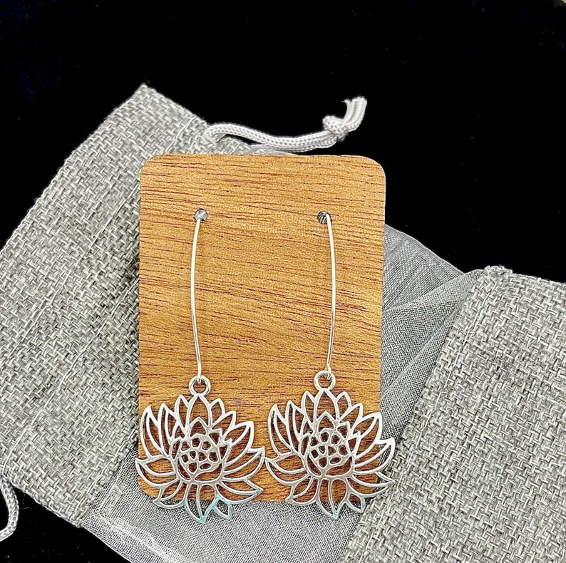 May include: A pair of silver dangle earrings with a delicate flower design. The earrings are displayed on a wooden stand.