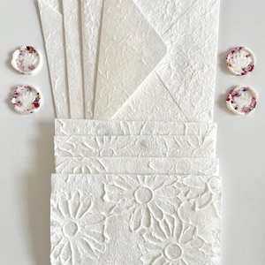 May include: A set of white stationery with floral embossed designs. The set includes envelopes and note cards. The envelopes have a textured surface and the note cards have a floral pattern.