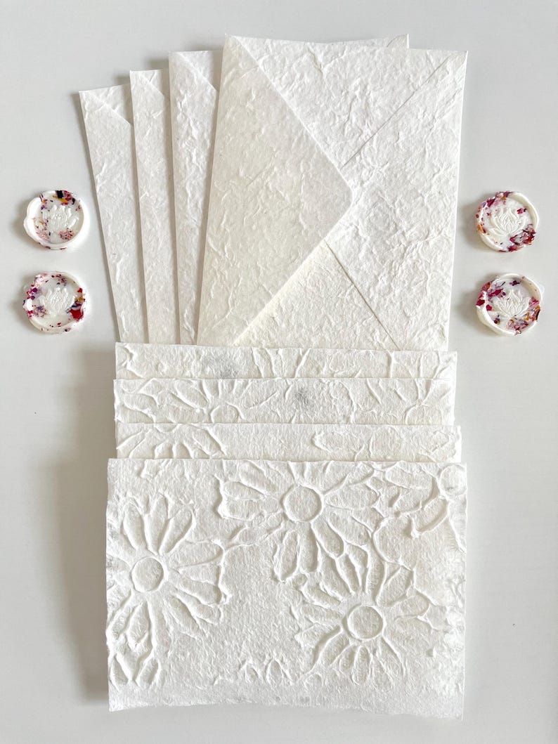 May include: A set of white stationery with floral embossed designs. The set includes envelopes and note cards. The envelopes have a textured surface and the note cards have a floral pattern.