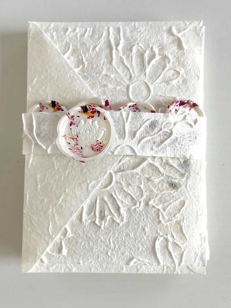 May include: White envelope with a decorative floral pattern and a wax seal with a floral design. The envelope is made of textured paper.