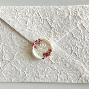 May include: White envelope with a textured surface and a wax seal with a floral design and colorful sprinkles.