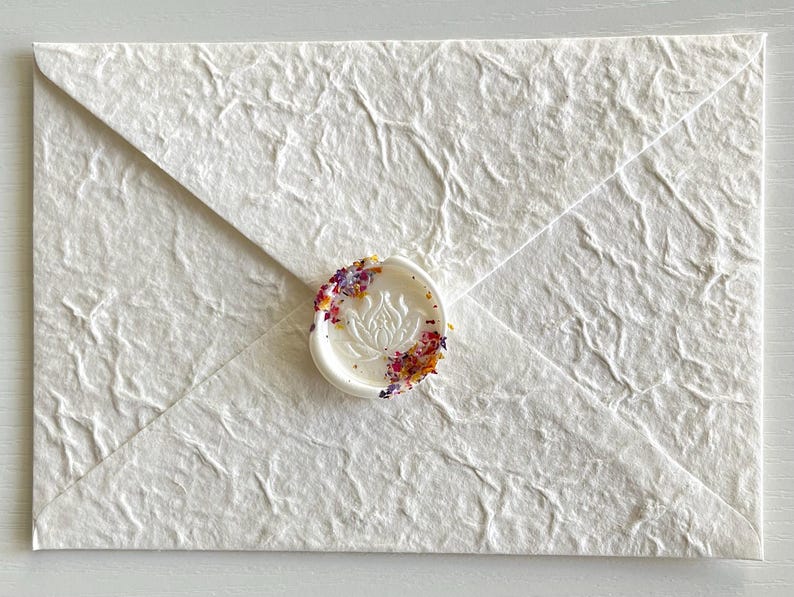 May include: White envelope with a textured surface and a wax seal with a floral design and colorful sprinkles.
