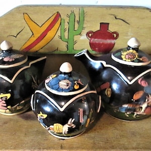 May include: A set of three black ceramic teapots with colorful painted designs. The teapots have white accents and feature scenes of people and animals.