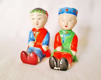Könnte beinhalten: Zwei Keramikfiguren von Menschen in traditioneller chinesischer Kleidung. Die Figur links trägt ein rotes und blaues Outfit mit einem blauen Hut. Die Figur rechts trägt ein grünes und rotes Outfit mit einem blauen Hut.