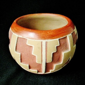 May include: A small, round, terracotta pot with a geometric design in shades of brown and beige. The pot is decorated with a repeating pattern of squares and rectangles.