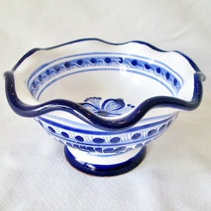 May include: A white ceramic bowl with a blue and white floral design and a scalloped rim. The bowl has a blue base and is perfect for serving snacks or desserts.