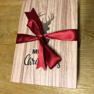 May include: A wooden gift box with a red ribbon and bow. The box has a woodgrain pattern and a deer silhouette with antlers. The text "Merry Christmas" is printed on the box.