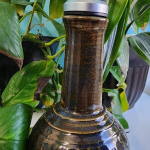 May include: A brown and blue ceramic bottle with a silver and black pour spout. The bottle has a textured surface and a round body.