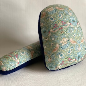 May include: Two decorative pillows with a blue and green floral pattern featuring birds and flowers. The pillows have a dark blue border. One pillow is cylindrical, and the other is a rounded rectangle.