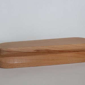 Op de afbeelding: Een rechthoekige houten doos met afgeronde randen. De doos is gemaakt van lichtgekleurd hout, mogelijk beuken of esdoorn, en heeft een natuurlijk houtnerfpatroon. Het ontwerp is eenvoudig en minimalistisch, met een glad, onversierd oppervlak.