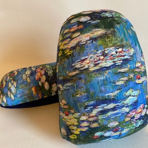 May include: Two fabric doorstops with a Monet-inspired water lily design. The doorstops are predominantly blue, with green, yellow, and pink accents, showing a tranquil water scene. One doorstop is upright, the other is horizontal.