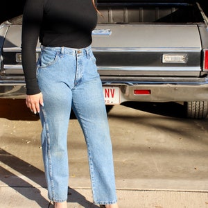 May include: A woman wearing a black mock neck top and blue jeans. She is standing in front of a grey pickup truck with a Nevada licence plate.
