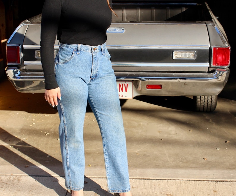 May include: A woman wearing a black mock neck top and blue jeans. She is standing in front of a grey pickup truck with a Nevada licence plate.