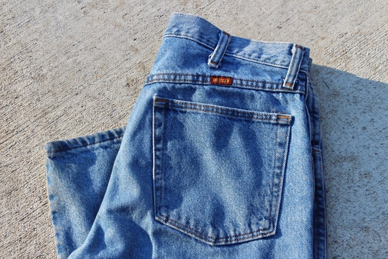 May include: A pair of blue denim jeans with a back pocket and a brown leather label that reads "Lee" on the back waistband.