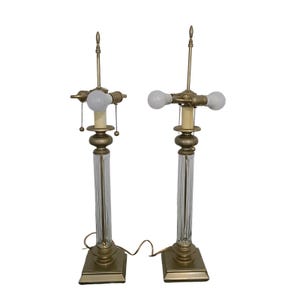 May include: A pair of gold table lamps with clear glass bases and three light bulbs each. The lamps have a traditional design and are perfect for adding a touch of elegance to any room.