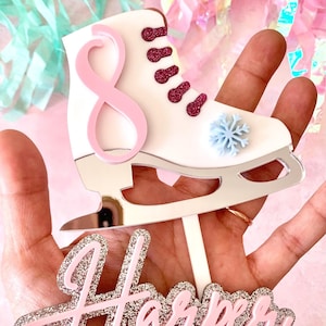 May include: A white and silver ice skate cake topper with a pink number 8 and the name "Harper" in pink and silver glitter.