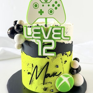 May include: A green and black birthday cake decorated with a green and white video game controller, the words "LEVEL 12", and the name "Max".