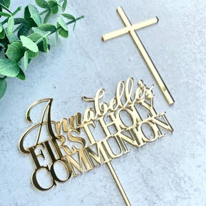 May include: Gold mirror acrylic cake topper with the text "Annabelle's First Holy Communion" and a gold cross.