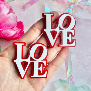 May include: Two white "LOVE" signs with red outlines. The signs are made of a thick, sturdy material and have a glossy finish.