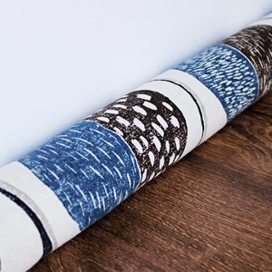 Puede incluir: Un tope de puerta enrollado con un fondo blanco y un patrón geométrico azul y marrón. El patrón presenta círculos y rayas.