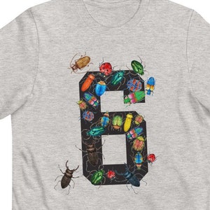K&ouml;nnte beinhalten: Ein graues T-Shirt mit einer schwarzen Zahl Sechs. Die Zahl besteht aus bunten K&auml;fern und Insekten.