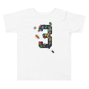 May include: White toddler t-shirt with a black number "3" made up of colorful beetles.