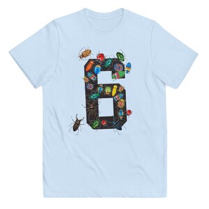 K&ouml;nnte beinhalten: Hellblaues T-Shirt mit einer schwarzen Zahl Sechs. Die Zahl ist mit bunten K&auml;fern und Insekten gef&uuml;llt.