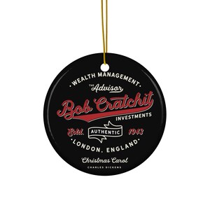 May include: A black Christmas ornament with gold string. The ornament features the text "Bob Cratchit Investments" in red and white, with additional text including "Christmas Carol" and "London, England."