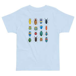 May include: A light blue t-shirt featuring a colourful pattern of 16 different beetles. The beetles are all different colours and have different patterns on their wings.