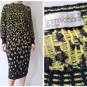 Puede incluir: Vestido de punto negro y amarillo con estampado de leopardo. El suéter tiene cuello redondo y mangas largas. La etiqueta dice "Gianni Versace Made in Italy".