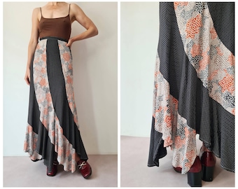 Könnte beinhalten: Ein langer, fließender Rock mit Patchwork-Design. Der Rock hat Bahnen aus schwarzen Polka-Dots, Blumenmuster in Orange und Weiß sowie durchgehende schwarze Streifen. Der Rock wird mit einem braunen Oberteil und bordeauxfarbenen Schuhen kombiniert.