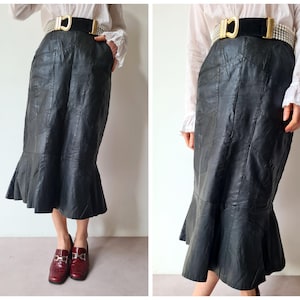 Op de afbeelding: Een zwarte leren rok met een zeemeerminzoom en een decoratieve gouden riem met strass. De rok is gemaakt van meerdere panelen leer en heeft een aansluitende pasvorm.