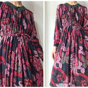 Könnte beinhalten: Langärmliges Kleid mit floralem Muster in Rosa-, Rot- und Lilatönen. Das Kleid hat einen dunkelblauen Hintergrund mit vertikalen Streifen und einen passenden Gürtel. Kragen und Manschetten sind dunkelgrün.