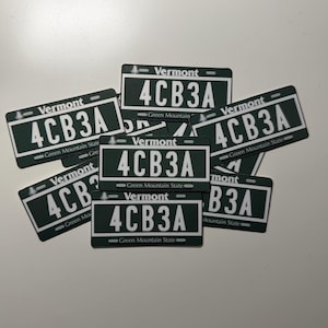 May include: A collection of rectangular stickers featuring a dark green background with white text. Each sticker displays the word Vermont at the top, the alphanumeric code 4CB3A in the center, and the phrase Green Mountain State at the bottom.