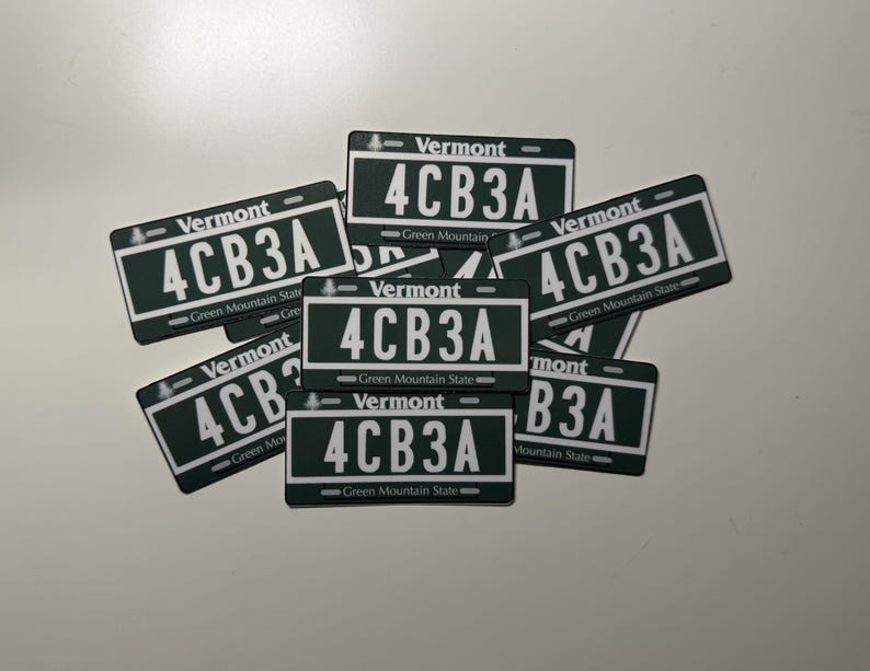 May include: A collection of rectangular stickers featuring a dark green background with white text. Each sticker displays the word Vermont at the top, the alphanumeric code 4CB3A in the center, and the phrase Green Mountain State at the bottom.