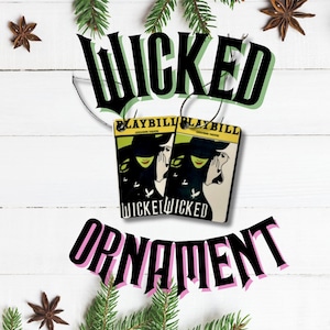 May include: Two ornaments with the word "WICKED" in black and green, and "ORNAMENT" in black and pink. The ornaments are shaped like playbills with a green witch and the text "WICKED" on them. The background is white with pine needles and star anise.