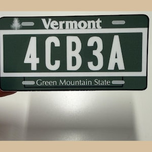 May include: A rectangular Vermont license plate sticker featuring a dark green background with white text. The plate displays the text Vermont at the top, the alphanumeric code 4CB3A in the center, and Green Mountain State at the bottom.