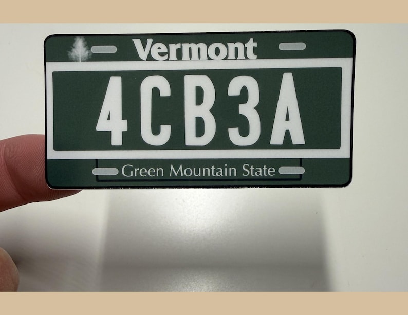 May include: A rectangular Vermont license plate sticker featuring a dark green background with white text. The plate displays the text Vermont at the top, the alphanumeric code 4CB3A in the center, and Green Mountain State at the bottom.