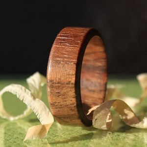 Könnte beinhalten: Nahaufnahme eines Holzrings in einem satten Braunton. Der Ring liegt auf einer grünen Oberfläche mit Holzspänen, die um ihn herum verstreut sind.