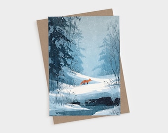 May include: A rectangular greeting card featuring an illustration of a small orange fox standing in a snowy forest landscape with blue-toned pine trees and a frozen stream, paired with a plain brown kraft paper envelope.