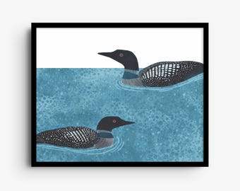 May include: A framed art print featuring two black and white loons swimming in textured blue water. The birds have spotted plumage, dark heads, and red eyes. The composition is set against a white background, enclosed in a black frame.
