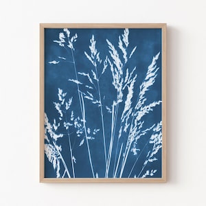 May include: A rectangular wall art print featuring a cyanotype-style botanical illustration of white grass stalks against a deep blue background, enclosed within a light-colored wooden frame with a clean, simple border design.