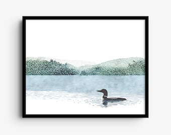 May include: A framed wall art print featuring a black loon swimming on a calm, light blue lake. In the background, a dense forest of green trees covers rolling hills under a white sky. The artwork is enclosed in a simple black frame.