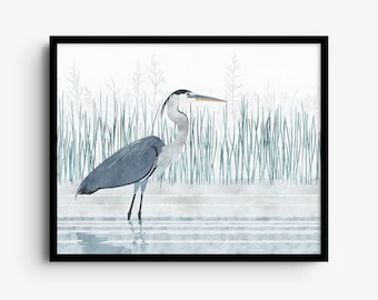 May include: A framed wall art print featuring a great blue heron standing in shallow water. The bird has slate gray feathers, a white neck, and a long yellow beak. Tall green reeds and grasses are visible in the background.