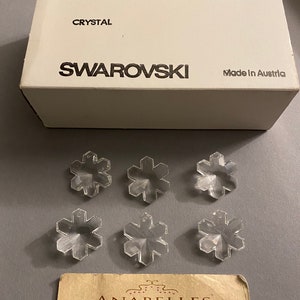 May include: Six clear crystal snowflake charms in a box labeled "Swarovski Crystal, Made in Austria". The box also has the text "Art. 6707, 25 MM, 2/12 Gross, Special".