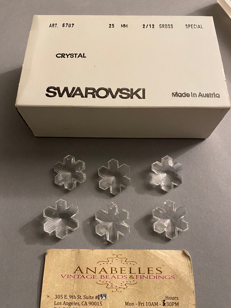 May include: Six clear crystal snowflake charms in a box labeled "Swarovski Crystal, Made in Austria". The box also has the text "Art. 6707, 25 MM, 2/12 Gross, Special".