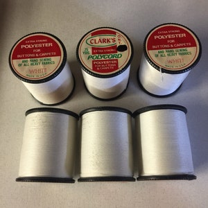 May include: Six spools of white extra strong polyester thread for buttons and carpets. The labels read Clark's O.N.T. 75 Yds. Polycord, Extra Strong Polyester for Buttons & Carpets and Hand Sewing of All Heavy Fabrics, White, Made in U.S.A.