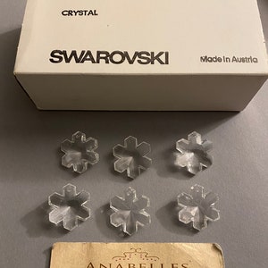 May include: Six clear crystal snowflake charms, each measuring 25 mm, packaged in a white box with the text "ART. 6707", "CRYSTAL", "SWAROVSKI", "2/12 GROSS", "SPECIAL", and "Made in Austria".