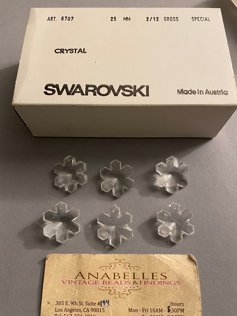 May include: Six clear crystal snowflake charms, each measuring 25 mm, packaged in a white box with the text "ART. 6707", "CRYSTAL", "SWAROVSKI", "2/12 GROSS", "SPECIAL", and "Made in Austria".